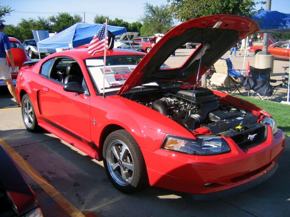 Red 2000 Ford Mustang coupe with hood open, showing engine and American flag on antenna