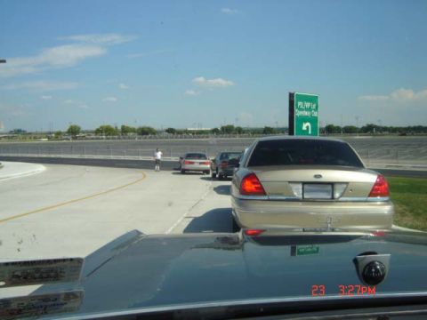 1988 Ford LTD Crown Victoria - A gold Ford Crown Victoria is seen from behind, with a speedway and a green sign in the background.