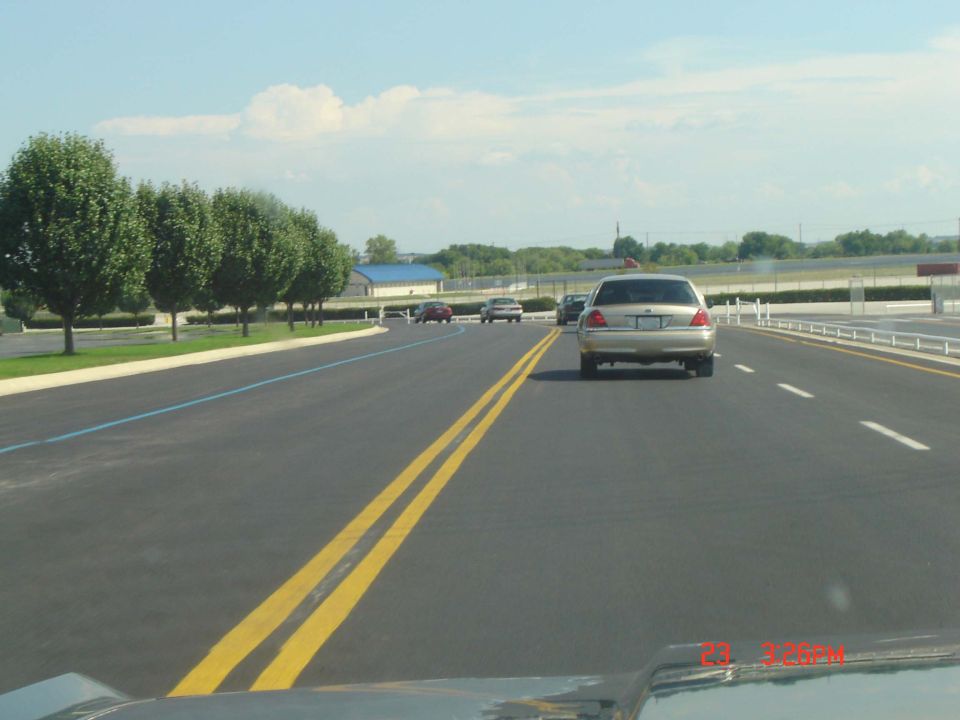 Silver Ford Crown Victoria driving on a highway, rear view. Visible text 'SUPERMOTORS'