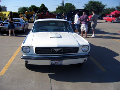 2000 Ford Crown Victoria - A white 1965 Ford Mustang is parked at a car show with other vehicles and people around.