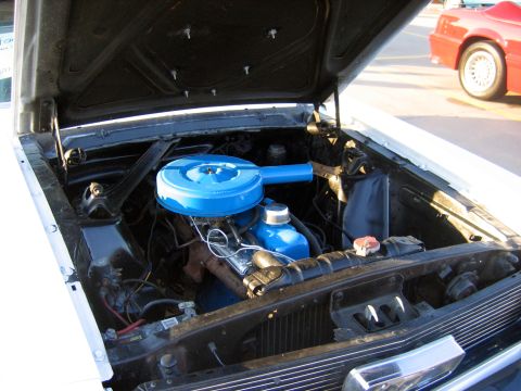 2000 Ford Crown Victoria - The engine bay of a classic car is shown, with a bright blue air filter assembly and a red car visible in the background.