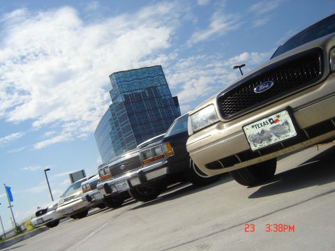 1988 Ford LTD Crown Victoria - Multiple Ford Crown Victorias parked in a lot, with a modern building in the background.