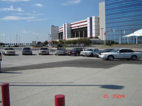 1988 Ford LTD Crown Victoria - A group of sedans are parked in a lot outside a large building. The white sedan on the right is likely a 1998 Ford Crown Victoria.