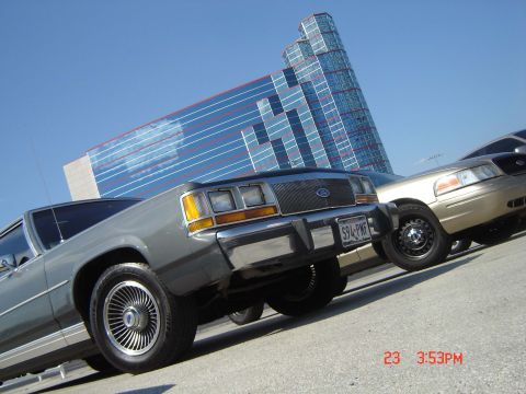 1988 Ford LTD Crown Victoria - Two Ford Crown Victorias are parked outside a modern building on a sunny day.