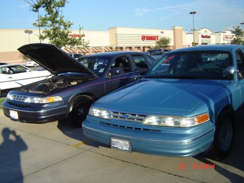 1988 Ford LTD Crown Victoria - Two Ford Crown Victorias, a blue and a dark blue model, are parked side-by-side with the hood of the dark blue one open.