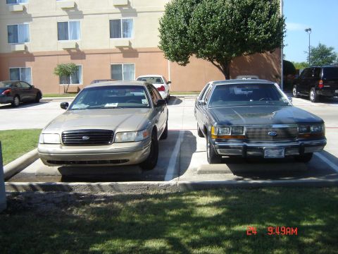 1988 Ford LTD Crown Victoria - Two Ford Crown Victorias are parked side-by-side in a hotel parking lot.