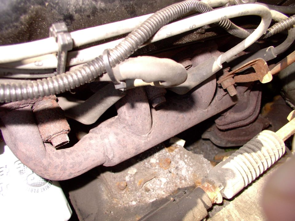 Rusty exhaust manifold, wiring loom, hoses and steering boot under the hood of a car