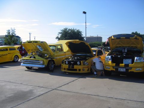 2000 Ford Crown Victoria - Multiple yellow vehicles, including a Ford F-150 truck, are displayed with their hoods open at an outdoor event.