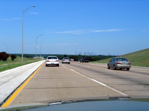 2000 Ford Crown Victoria - A view from a car driving on a highway with other vehicles and a distant city skyline under a clear blue sky.