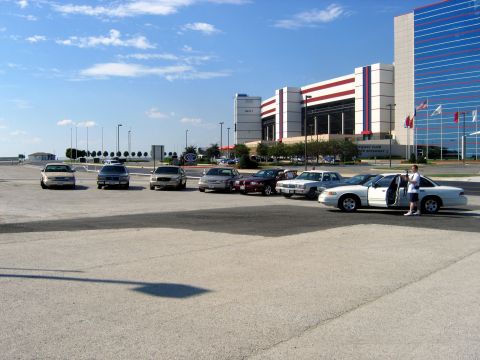 2000 Ford Crown Victoria - A group of sedans are parked in a lot with a large stadium in the background.