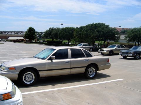2000 Ford Crown Victoria - A tan sedan is parked in a lot with other vehicles under a partly cloudy sky.