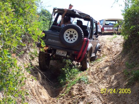 1987 Ford Bronco - Two off-road vehicles navigate a steep, muddy trail surrounded by dense vegetation.