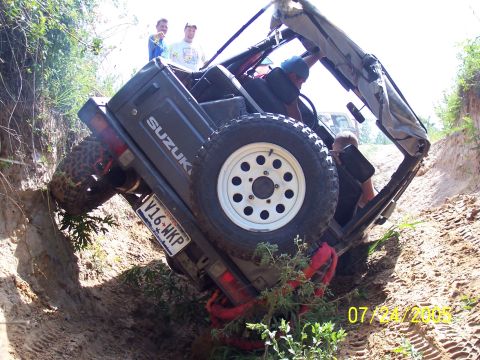 1987 Ford Bronco - A Suzuki Samurai is stuck at an extreme angle in a dirt ditch, with occupants inside.