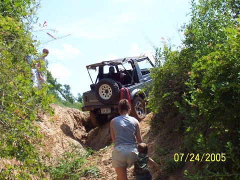 1987 Ford Bronco - Suzuki Samurai navigates a steep dirt trail on a sunny day.