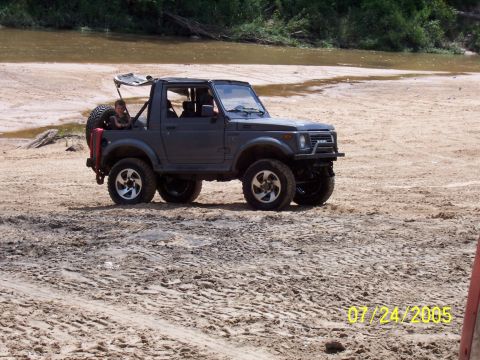 1987 Ford Bronco - An off-road SUV is seen parked on a sandy bank next to a body of water.