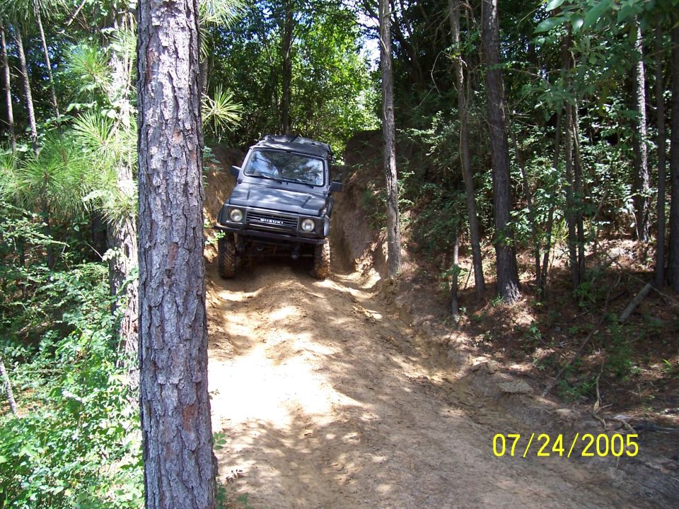 Suzuki Samurai climbing a dirt hill in a wooded area