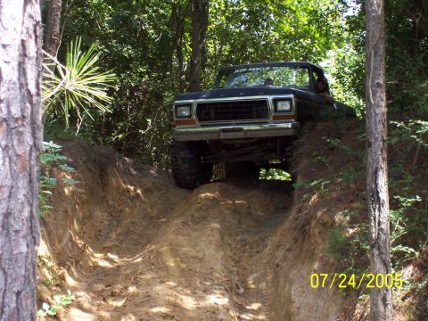 1987 Ford Bronco - A black Ford truck navigates a steep dirt trail in a wooded area.