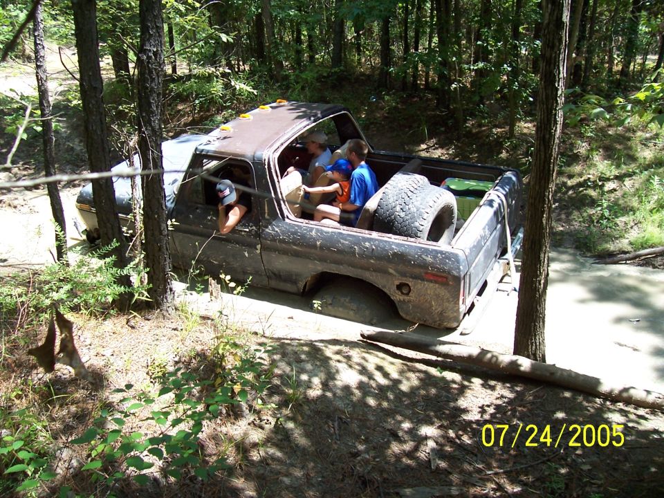 Muddy truck with people inside stuck in a wooded area, spare tire in the bed