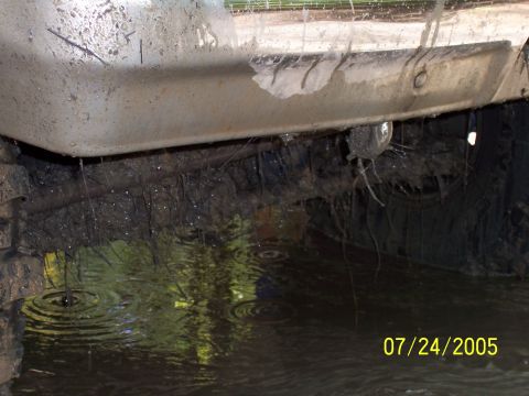 1987 Ford Bronco - The vehicle's undercarriage is submerged in murky water and mud, with debris hanging from it.