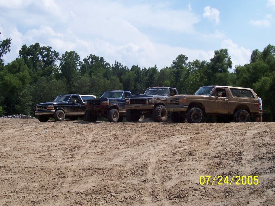 Tan 1987 Ford Bronco parked with three trucks on a dirt track
