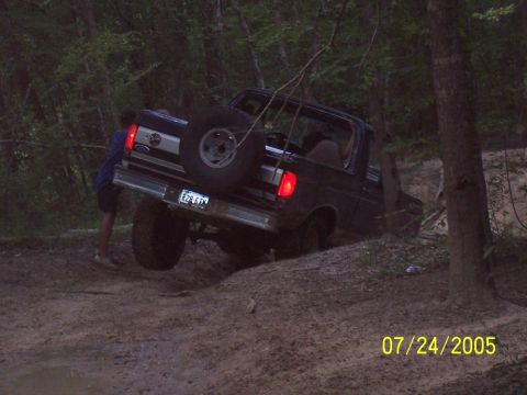1987 Ford Bronco - 1987 Ford Bronco navigating a challenging off-road trail with assistance.