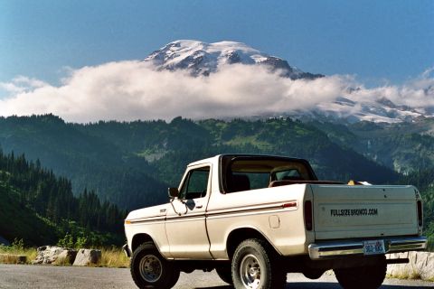 1979 Ford Bronco - A white 1979 Ford Bronco is parked on a roadside with a , cloud-shrouded mountain range in the background.