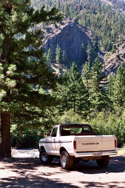 1979 Ford Bronco - A classic Ford Bronco sits parked in a scenic, wooded mountain area, with a rocky cliff face in the background.