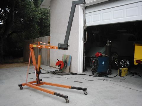 1978 Ford Bronco - An engine hoist stands ready in front of a garage containing a car, welding gear, and other automotive parts.
