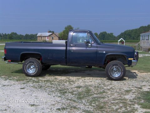1986 GMC C/K Pickup - This dark blue pickup truck appears to be from the 1980s, with a lifted suspension and off-road tires.