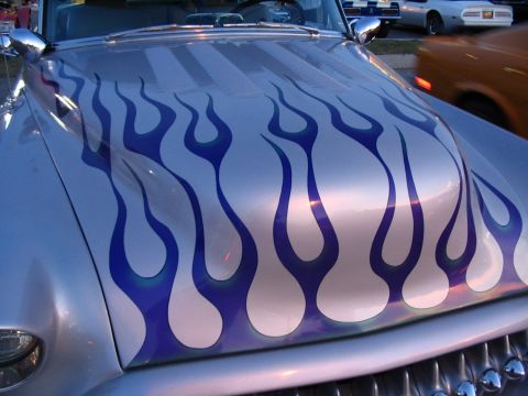 1993 Ford Taurus - A silver car with blue flame graphics on the hood is parked at a car show with other vehicles around.