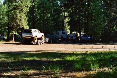 1979 Ford Bronco - A lifted white SUV is loaded onto a trailer at a wooded campsite with multiple other vehicles present.
