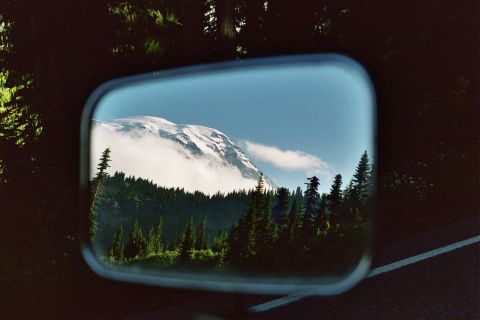 1979 Ford Bronco - A mountain scene is reflected in the side mirror of a vehicle, showing a snow-capped peak and dense forest.