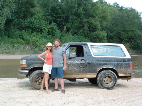1993 Ford Bronco - A couple poses with their muddy 1993 Ford Bronco near a body of water.