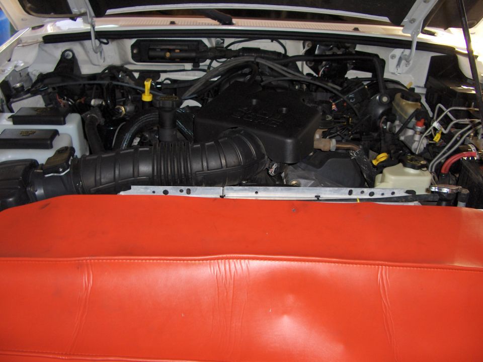 Engine bay of white Ford Ranger showing black DOHC engine cover, intake hose, and red fender cover.