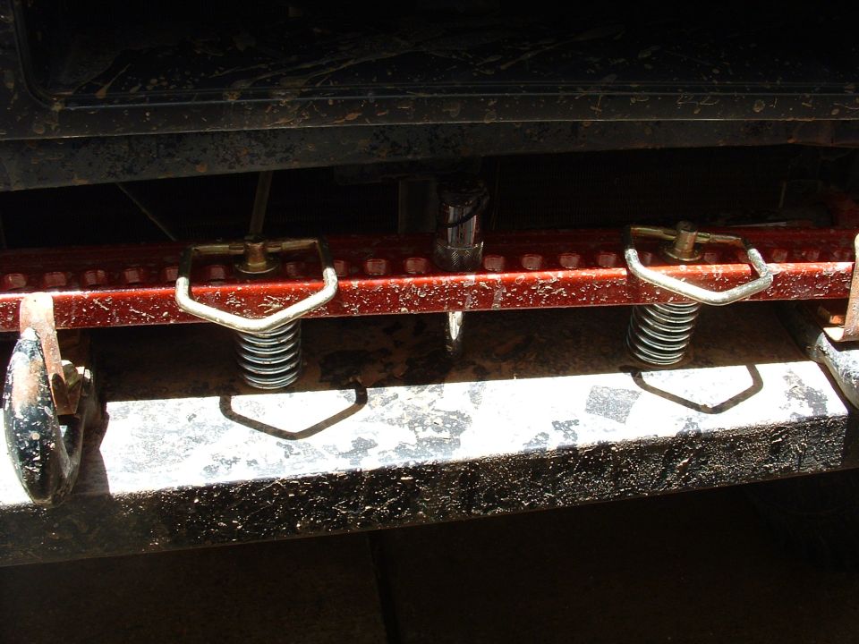 Two spring-loaded latch hooks bolted to a red slotted steel rail on a muddy vehicle
