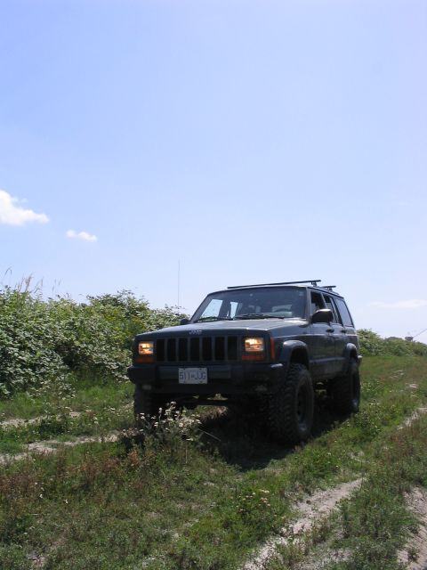 2000 Jeep Cherokee - A dark Jeep Cherokee drives off-road on a sunny day, its body style clearly indicating a 2000 model year.