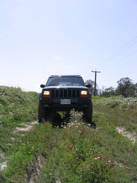 2000 Jeep Cherokee - A 2000 Jeep Cherokee drives on a grassy, unpaved path under a clear blue sky.