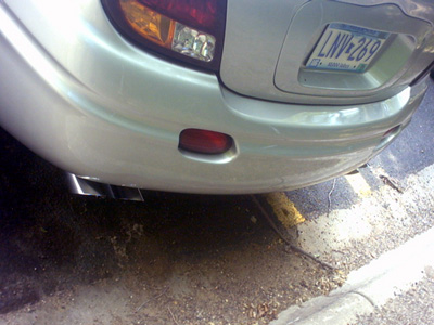 2002 Oldsmobile Aurora - The rear of a silver 2002 Oldsmobile Aurora is visible, showing the bumper, taillight, and dual exhaust pipes.