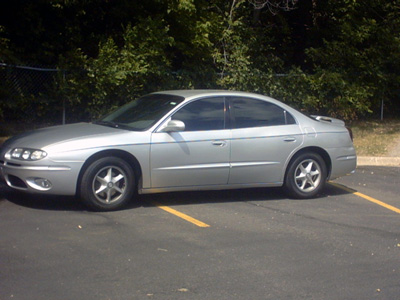 2002 Oldsmobile Aurora - A silver sedan is parked in a lot with trees in the background.