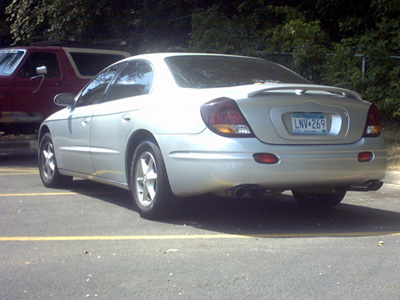 2002 Oldsmobile Aurora - A silver sedan with a spoiler is parked in a lot next to a red SUV.