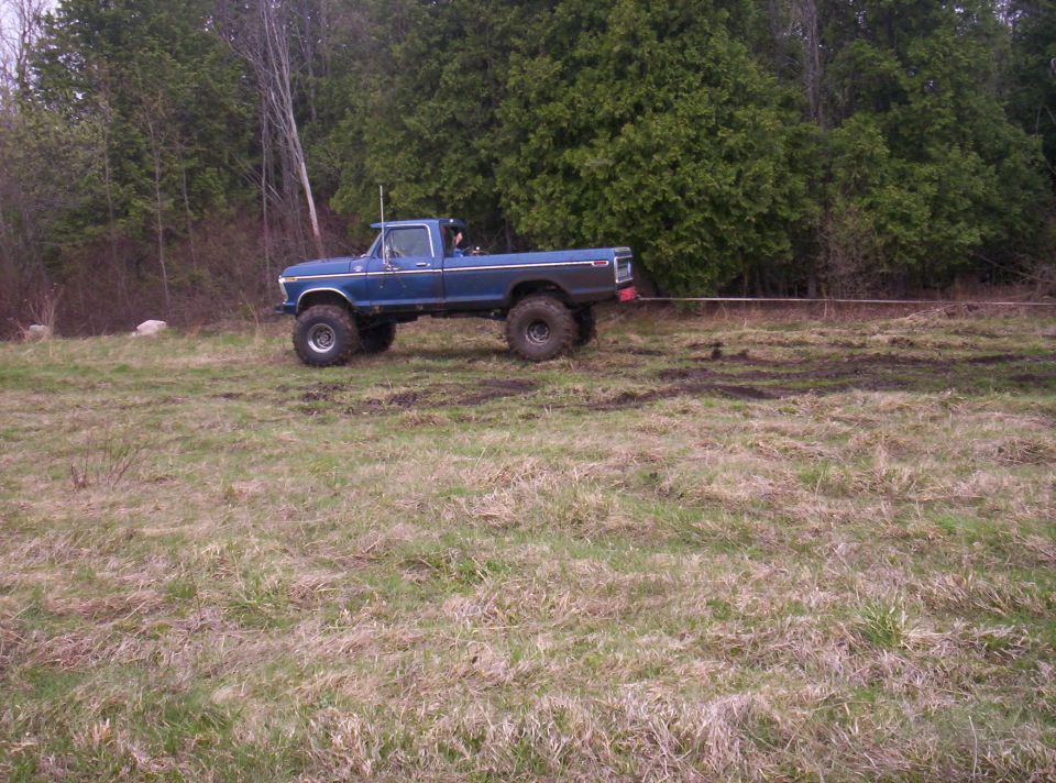 Side view of blue lifted pickup truck being towed in a grassy field