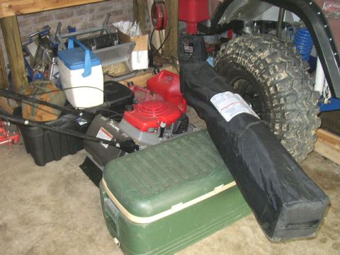 1995 Ford Bronco - A large off-road tire and suspension parts are visible among various stored items in a garage.