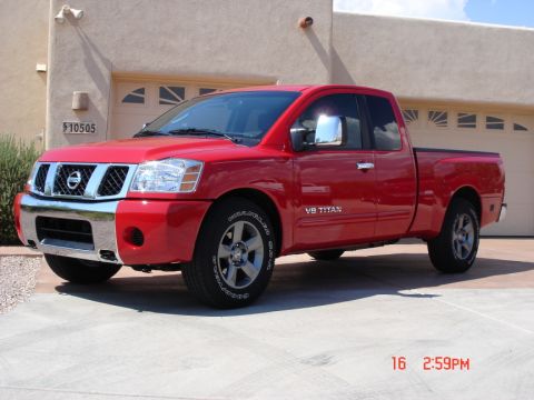 2005 Nissan Titan - This red Nissan Titan pickup truck is parked in front of a residential garage.
