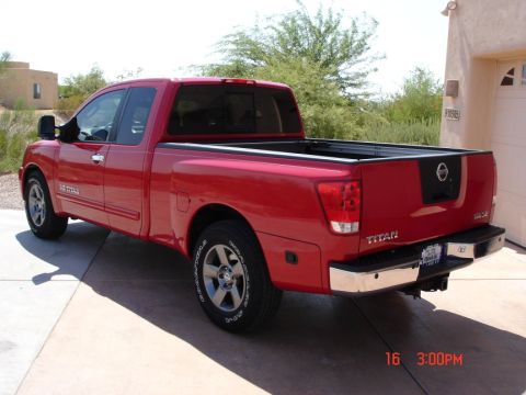 2005 Nissan Titan - This red 2005 Nissan Titan pickup truck is seen from a three-quarter front angle, parked on a paved surface in front of a garage.