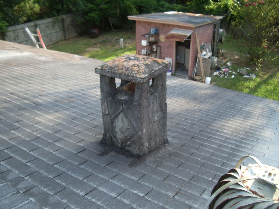 chimney on a shingled roof, with a brick shed in the background