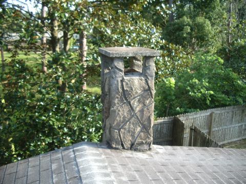 1978 Ford Bronco - A stone chimney stands on a rooftop, surrounded by greenery and a wooden fence.