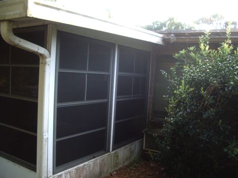 1978 Ford Bronco - Exterior view of a screened-in porch with a downspout and overgrown shrubbery.