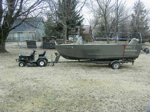 1991 Ford Bronco - A lawn tractor is connected to a boat trailer, which holds a green boat with 'JUCKS NIGHTMARE' written on its side.