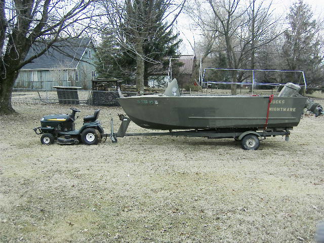 Olive aluminum duck boat lettered DUCKS NIGHTMARE on trailer, riding mower alongside