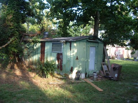 1978 Ford Bronco - A weathered green shed sits in a yard with trees and grass, showing signs of disrepair.